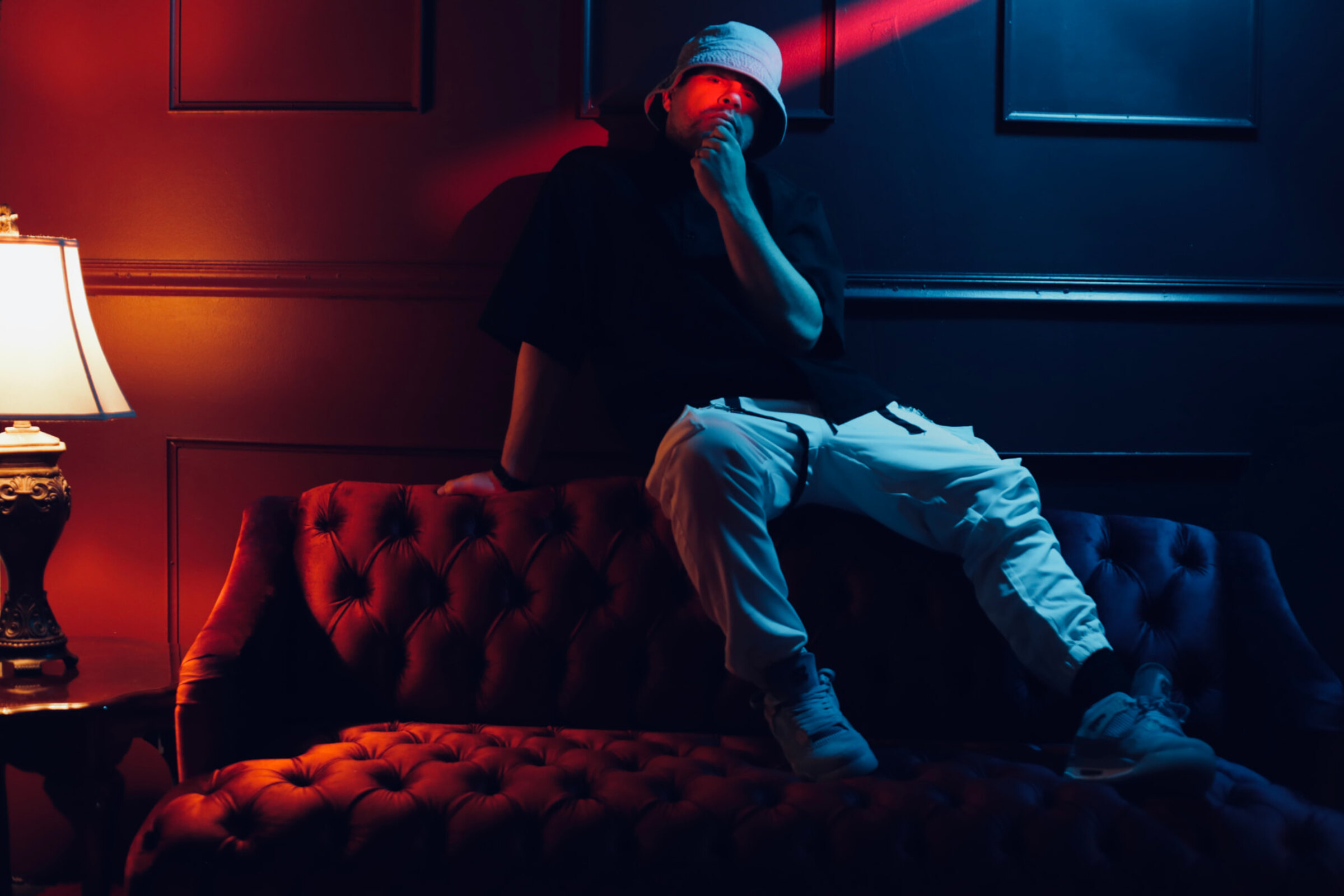 Gustavo Ortega seated on a velvet couch under red and blue cinematic lighting